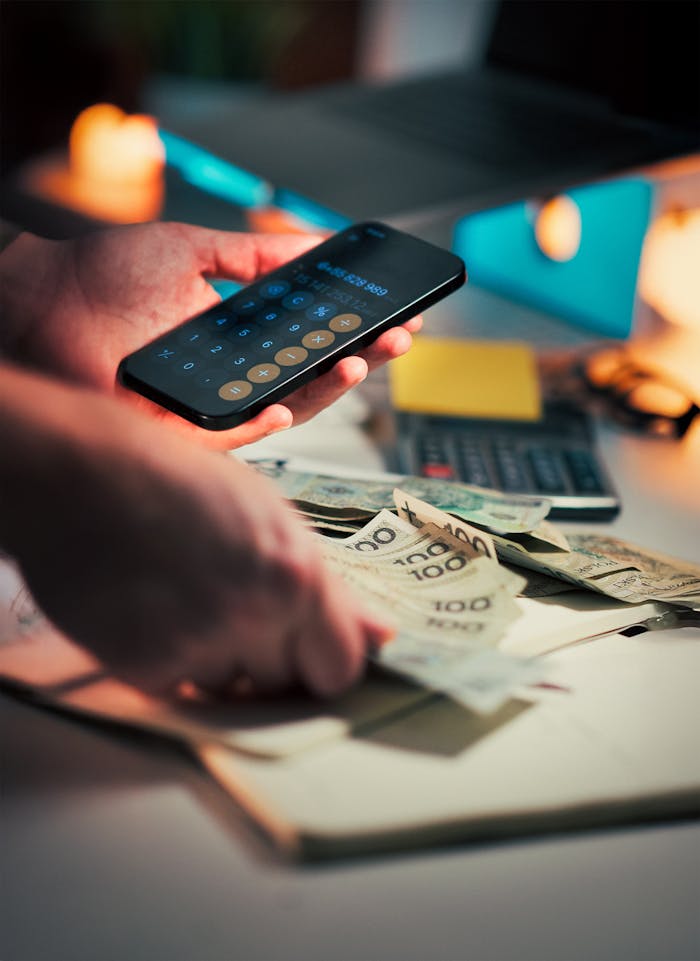 Hands using a smartphone calculator and handling cash on a desk, suggesting financial planning.